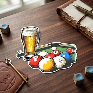 May include: A sticker illustration featuring a tall glass of golden beer with white foam positioned next to a green pool table surface covered with various colored billiard balls, including a yellow ball, a red eight ball, and a blue ball.