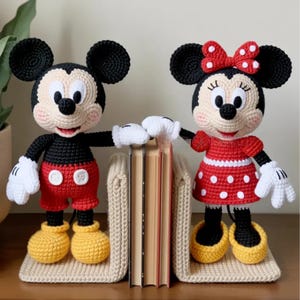 Könnte beinhalten: Gehäkelte Mickey- und Minnie-Mouse-Buchstützen. Mickey trägt rote Shorts, ein schwarzes Hemd und gelbe Schuhe. Minnie trägt ein rotes Polka-Dot-Kleid und eine Schleife, schwarze Schuhe. Beide haben weiße Handschuhe und stehen auf beigen Buchstützen.