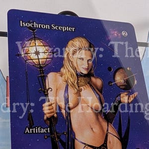 May include: A Magic: The Gathering card titled "Isochron Scepter." The card features a fantasy illustration of a woman holding a staff with a glowing orb. The background is a deep purple with stars and planets. The card is an artifact.