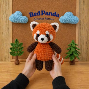 May include: A crocheted red panda plush toy with brown arms and legs, white accents, and a striped tail. The text "Red Panda Crochet Pattern" is above the plush. Two blue cloud and two green tree crochet decorations are in the background.