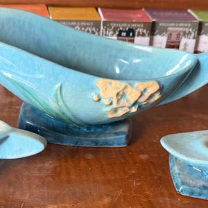 Puede incluir: Un centro de mesa de cerámica turquesa y dos ceniceros a juego. El cuenco tiene un diseño único y fluido con un adorno floral en relieve. Los ceniceros tienen una forma similar con una abertura circular. Un conjunto de decoración del hogar vintage.