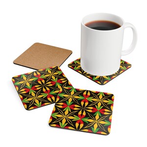 May include: A white ceramic mug filled with coffee sits on a square coaster with a black background and a repeating floral pattern in yellow, red, and green. Two additional coasters with the same design are visible.