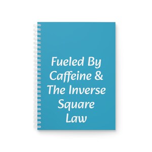 Op de afbeelding: Een spiraalgebonden notitieboek met een turquoise omslag. De omslag heeft de witte tekst "Fueled By Caffeine & The Inverse Square Law". Het notitieboek heeft een witte spiraalbinding.