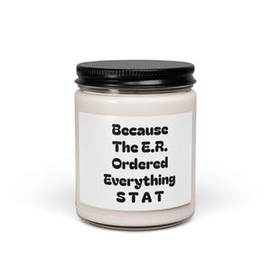 Può includere: Una candela bianca in un barattolo di vetro con coperchio nero. L'etichetta presenta il testo "Because The E.R. Ordered Everything STAT" in grassetto nero. Candela profumata per la casa.