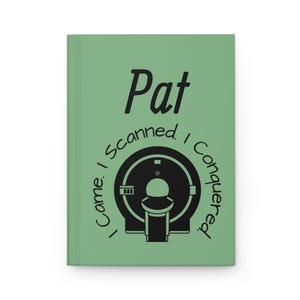 Op de afbeelding: Een saliegroen notitieboek met het woord "Pat" boven een zwarte illustratie van een MRI-machine. De tekst "Came. I Scanned. I Conquered." is in een halve cirkel rond de MRI-machine gedrukt.