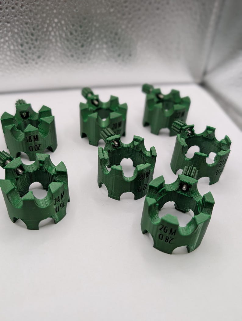 May include: A collection of seven green, gear-shaped components. Each component has a series of teeth around the outer edge and a small, cylindrical piece on top. The components are labeled with white text, including numbers and letters.