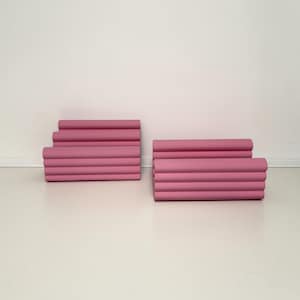 Może przedstawiać: Dwa zestawy r&oacute;żowych, cylindrycznych obiekt&oacute;w ułożonych w stos. Każdy zestaw składa się z wielu poziomych cylindr&oacute;w, tworząc efekt warstwowy. Obiekty mają jednolity, stonowany r&oacute;żowy kolor i są umieszczone na białej powierzchni.