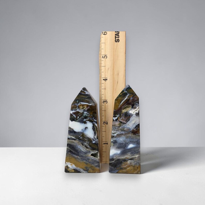 Puede incluir: Dos obeliscos de piedra pulida con una regla para la escala. Los obeliscos miden aproximadamente 7,6 cm de altura y presentan una mezcla de colores marr&oacute;n, blanco y gris. La regla es de madera con marcas negras.