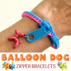 May include: A blue and pink zipper bracelet with a pink balloon dog charm. The bracelet is on a wrist. The text "BALLOON DOG ZIPPER BRACELETS" is at the bottom of the image.