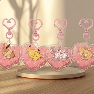 Puede incluir: Cuatro llaveros en forma de corazón con detalles en rosa. Cada llavero presenta un personaje de dibujos animados diferente durmiendo sobre una almohada rosa. Los llaveros tienen cierres en forma de corazón rosa.