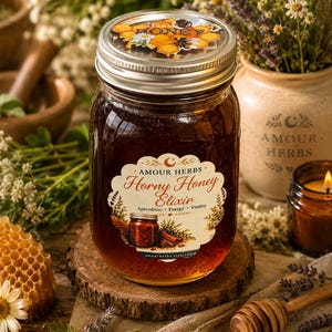 Può includere: Un barattolo di vetro riempito di miele color ambra scuro, con un coperchio argentato decorato con un motivo a nido d'ape. L'etichetta riporta Amour Herbs Horny Honey Elixir, Aphrodisiac, Energy, Vitality e un'illustrazione di un barattolo.