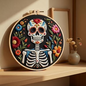 May include: Embroidered Day of the Dead skull art in a wooden hoop. The skull is white with colorful floral details, surrounded by vibrant flowers and foliage on a black background. The skeleton's rib cage is blue.