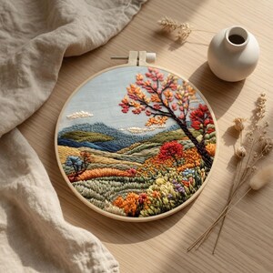 Peut inclure: Broderie d'art détaillée dans un cercle en bois, représentant un paysage automnal. L'œuvre présente un arbre aux couleurs vives, des collines et un ciel bleu. Les couleurs sont riches et les détails précis.