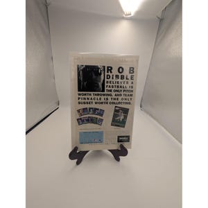 May include: A baseball card display featuring a card with the text "ROB DIBBLE BELIEVES A FASTBALL IS THE ONLY PITCH WORTH THROWING. AND TEAM PINNACLE IS THE ONLY SUBSET WORTH COLLECTING." The display is held by a black stand.