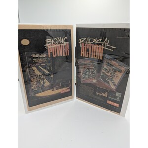 May include: Two vintage Capcom video game advertisements displayed in protective sleeves. The left print features Bionic Commando with the text Bionic Power. The right print features Mega Man and Strider with the text Radical Action.