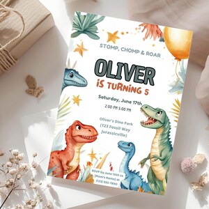 May include: A rectangular birthday invitation card featuring watercolor illustrations of three dinosaurs in red, blue, and green. The text reads: STOMP, CHOMP & ROAR, OLIVER IS TURNING 5, Saturday, June 17th, 2:00 PM 5:00 PM, Oliver's Dino Park, 123 Fossil Way, Jurassicville, RSVP by June 10th to [Mom's Name] at (123) 555-7890.