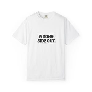 Puede incluir: Camiseta blanca con el texto "WRONG SIDE OUT" en un recuadro negro en la parte delantera. La camiseta tiene cuello redondo y mangas cortas. La prenda está hecha de un material suave y cómodo.