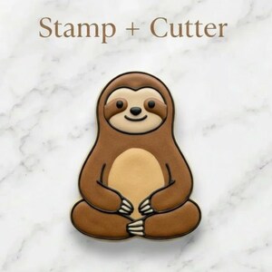 May include: A brown sloth-shaped cookie cutter and stamp set. The sloth is sitting with its legs crossed and has a light brown belly. The text "Stamp + Cutter" is above the sloth. The background is a white marble pattern.