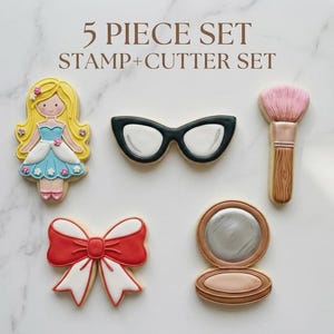 May include: A five-piece cookie cutter set with a princess, sunglasses, makeup brush, bow, and compact. The princess has a yellow hair, blue dress, and pink shoes. The sunglasses are black and white. The makeup brush has a pink brush and wooden handle.