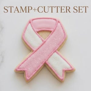 May include: A cookie shaped like a awareness ribbon with pink and white icing and a sparkling sugar finish. The text STAMP+CUTTER SET is printed above the cookie. The ribbon features a pink outline and alternating pink and white sections.
