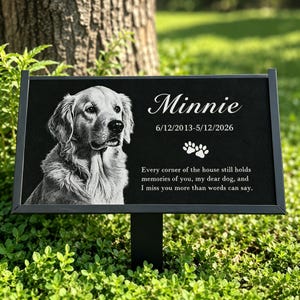 May include: A black rectangular memorial plaque featuring a white engraved portrait of a dog, the name Minnie, the dates 6/12/2013-5/12/2026, two paw prints, and the text: Every corner of the house still holds memories of you, my dear dog, and I miss you more than words can say.