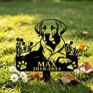 May include: Black metal garden stake with a Labrador Retriever design. The stake displays the name "MAX" and the years "2010-2024", along with paw prints. The artwork is set against a backdrop of green grass and flowers.