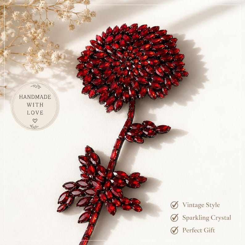 Puede incluir: Un broche decorativo con forma de flor, cubierto totalmente por cristales de color rojo oscuro con talla marquesa. El dise&ntilde;o presenta una flor central con tallo y hojas, todo incrustado con piedras rojas facetadas que crean un efecto brillante.