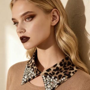 May include: A tan-colored top with a detachable collar. The collar features a leopard print pattern and is embellished with numerous clear, sparkling rhinestones. The model has blonde hair and dark lipstick.