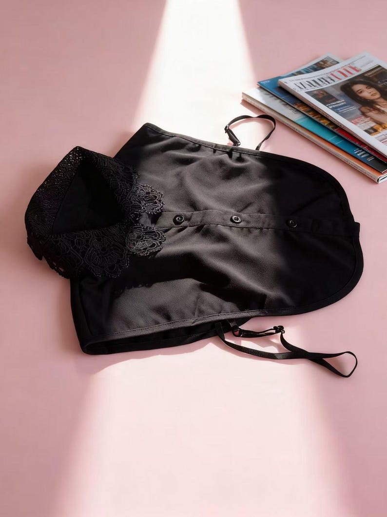 May include: Black sleepwear set with lace trim on the top and adjustable straps. The set includes a top with buttons and a matching bottom. The sleepwear is displayed on a pink surface with magazines in the background.