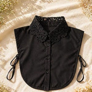 May include: A black detachable collar with a lace trim. The collar has a button-down front and tie closures on each side. The collar is made of a smooth, solid black fabric.