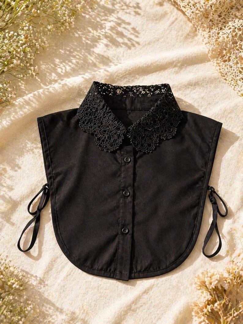 May include: A black detachable collar with a lace trim. The collar has a button-down front and tie closures on each side. The collar is made of a smooth, solid black fabric.