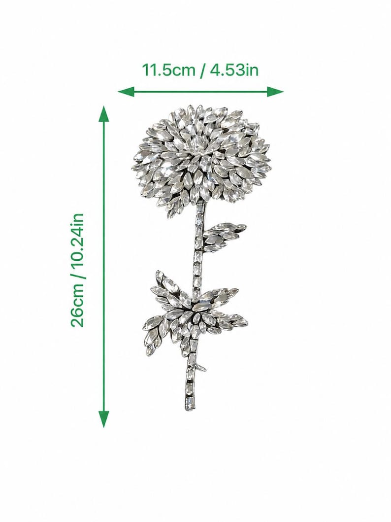 Puede incluir: Un adorno floral de tono plateado incrustado con cristales transparentes, que presenta una gran flor circular y un tallo con hojas. El art&iacute;culo mide 11,5 cm de ancho y 26 cm de alto, seg&uacute;n lo indicado por las marcas de medici&oacute;n visibles.