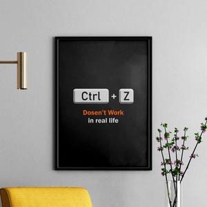 Puede incluir: Arte de pared enmarcado en negro con el texto "Ctrl + Z Doesn't Work in real life" en blanco y naranja. La obra de arte presenta las teclas Ctrl y Z de un teclado. Una silla amarilla y un jarrón de flores están en el fondo.