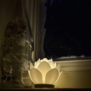 Puede incluir: Una taza de cerámica blanca con un asa negra y el texto "But First, Coffee" en un estilo manuscrito. La taza está sobre una superficie blanca. La taza mide aproximadamente 10 cm de alto.