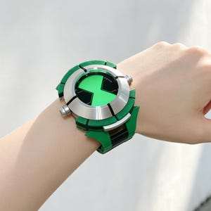 Puede incluir: Un reloj de pulsera con una esfera circular que presenta un centro verde brillante y un símbolo negro en forma de reloj de arena. El reloj tiene un bisel de plata metálica y una correa gruesa de color verde vibrante con detalles en negro.