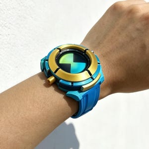 May include: A wrist-worn device featuring a circular gold-colored bezel and a blue frame. The center display shows a black and green geometric pattern. The band is a solid blue color with a textured surface, secured with a side-mounted gold button.