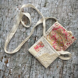 SMALL HAND STITCHED NECKLACE
Beautifully hand stitched pouch to hold your precious memories, a photograph or crystals. Made by slow stitching vintage French linens, lace, silk and quilting fabrics in shades of cream and white, lined with a pretty pink vintage paisley cotton, embellished with small silver bugle beads and a vintage fabric flower. 
It has a simple fold over top with a raw edged cream sari silk ribbon to wear around the neck.
Pouch: 3+1/4" / 8 cm square.
Ribbon drop: 16+1/2" / 42 cm
