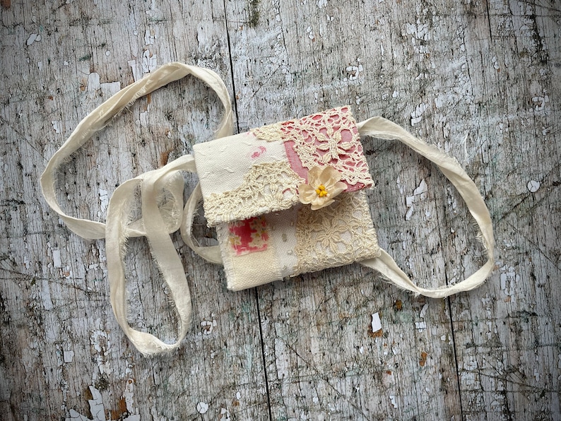 SMALL HAND STITCHED NECKLACE
Beautifully hand stitched pouch to hold your precious memories, a photograph or crystals. Made by slow stitching vintage French linens, lace, silk and quilting fabrics in shades of cream and white, lined with a pretty pink vintage paisley cotton, embellished with small silver bugle beads and a vintage fabric flower. 
It has a simple fold over top with a raw edged cream sari silk ribbon to wear around the neck.
Pouch: 3+1/4" / 8 cm square.
Ribbon drop: 16+1/2" / 42 cm
