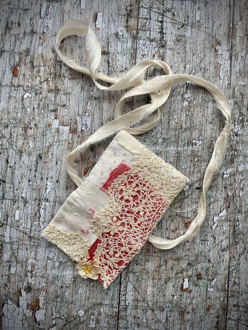SMALL HAND STITCHED NECKLACE
Beautifully hand stitched pouch to hold your precious memories, a photograph or crystals. Made by slow stitching vintage French linens, lace, silk and quilting fabrics in shades of cream and white, lined with a pretty pink vintage paisley cotton, embellished with small silver bugle beads and a vintage fabric flower. 
It has a simple fold over top with a raw edged cream sari silk ribbon to wear around the neck.
Pouch: 3+1/4" / 8 cm square.
Ribbon drop: 16+1/2" / 42 cm