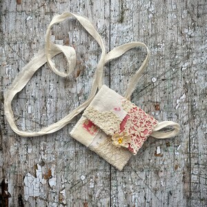 SMALL HAND STITCHED NECKLACE
Beautifully hand stitched pouch to hold your precious memories, a photograph or crystals. Made by slow stitching vintage French linens, lace, silk and quilting fabrics in shades of cream and white, lined with a pretty pink vintage paisley cotton, embellished with small silver bugle beads and a vintage fabric flower. 
It has a simple fold over top with a raw edged cream sari silk ribbon to wear around the neck.
Pouch: 3+1/4" / 8 cm square.
Ribbon drop: 16+1/2" / 42 cm