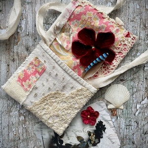 SMALL HAND STITCHED NECKLACE
Beautifully hand stitched pouch to hold your precious memories, a photograph or crystals. Made by slow stitching vintage French linens, lace, silk and quilting fabrics in shades of cream and white, lined with a pretty pink vintage paisley cotton, embellished with small silver bugle beads and a vintage fabric flower. 
It has a simple fold over top with a raw edged cream sari silk ribbon to wear around the neck.
Pouch: 3+1/4" / 8 cm square.
Ribbon drop: 16+1/2" / 42 cm