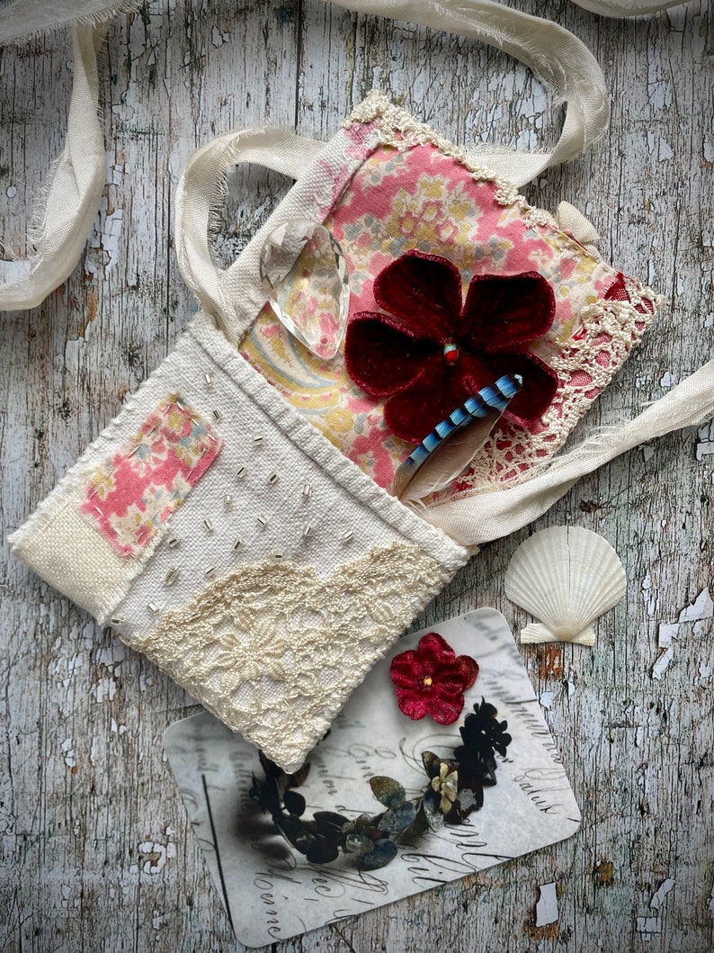 SMALL HAND STITCHED NECKLACE
Beautifully hand stitched pouch to hold your precious memories, a photograph or crystals. Made by slow stitching vintage French linens, lace, silk and quilting fabrics in shades of cream and white, lined with a pretty pink vintage paisley cotton, embellished with small silver bugle beads and a vintage fabric flower. 
It has a simple fold over top with a raw edged cream sari silk ribbon to wear around the neck.
Pouch: 3+1/4" / 8 cm square.
Ribbon drop: 16+1/2" / 42 cm