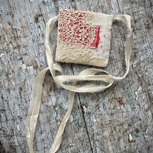 SMALL HAND STITCHED NECKLACE
Beautifully hand stitched pouch to hold your precious memories, a photograph or crystals. Made by slow stitching vintage French linens, lace, silk and quilting fabrics in shades of cream and white, lined with a pretty pink vintage paisley cotton, embellished with small silver bugle beads and a vintage fabric flower. 
It has a simple fold over top with a raw edged cream sari silk ribbon to wear around the neck.
Pouch: 3+1/4" / 8 cm square.
Ribbon drop: 16+1/2" / 42 cm