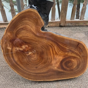 May include: A unique, handcrafted wooden bowl with a natural edge. The bowl features a rich, warm brown color with visible wood grain patterns and a glossy black resin accent on one side. The bowl's organic shape adds a touch of rustic elegance.