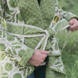 May include: A green and white quilted robe with a floral pattern. The robe is tied at the waist with a matching belt. The robe's design features a repeating pattern of green dandelions on a white background.