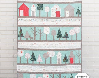 May include: A quilt pattern called "Through the Woods" designed by Rachel Rossi. The quilt features a repeating pattern of houses, trees, and deer in a woodland setting. The quilt is made with a variety of fabrics in shades of red, green, brown, and white.