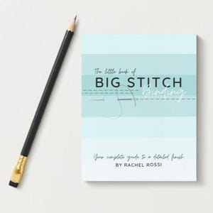 Könnte beinhalten: Ein Buch mit dem Titel "The little book of BIG STITCH Binding" mit hellblau-weißem Einband, neben einem schwarzen Bleistift mit goldener Zwinge. Das Buchcover zeigt Text und eine Nadel- und Fadenillustration.