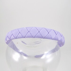 May include: A lavender braided headband made of satin ribbon. The headband is designed with a diamond pattern.