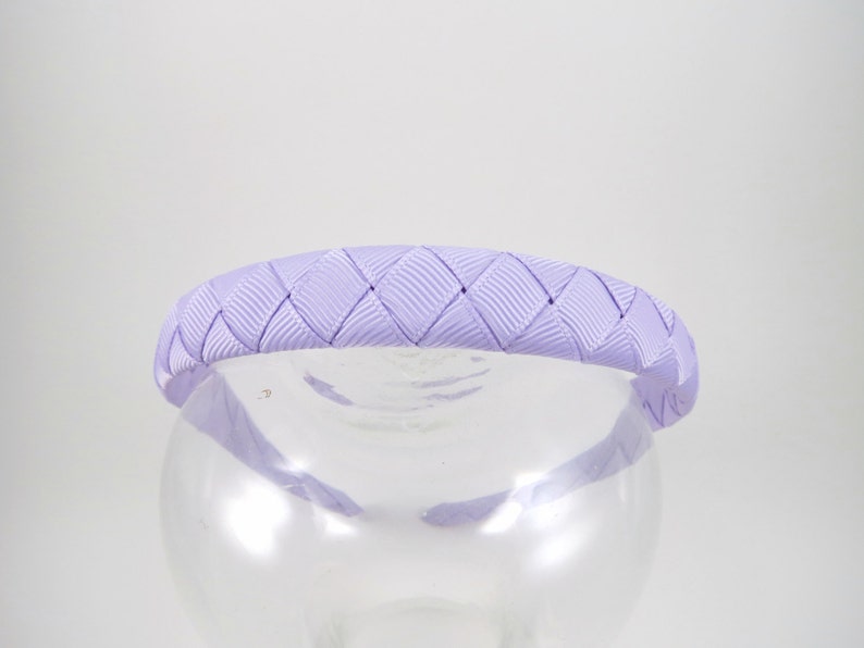 May include: A lavender braided headband made of satin ribbon. The headband is designed with a diamond pattern.
