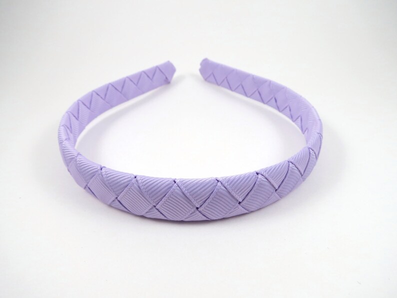 May include: A lavender braided headband for hair. The headband is made of a woven ribbon.